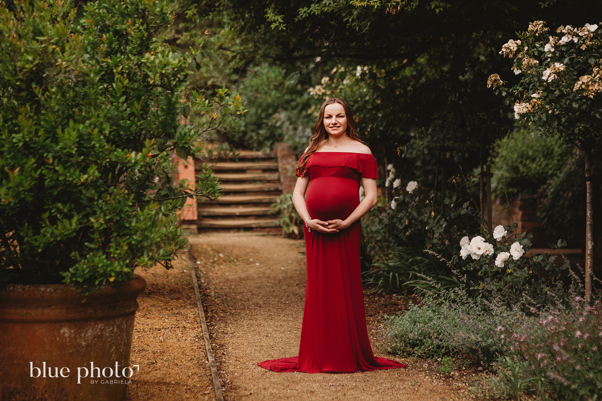 A pregnant lady in red dress is posing in The Hill Garden and Pergola, North London. 